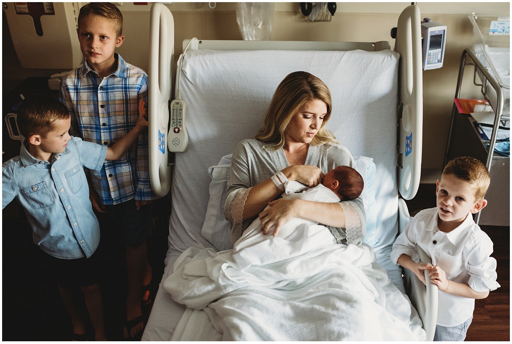 3 curious little brothers around new baby boy in moms arms