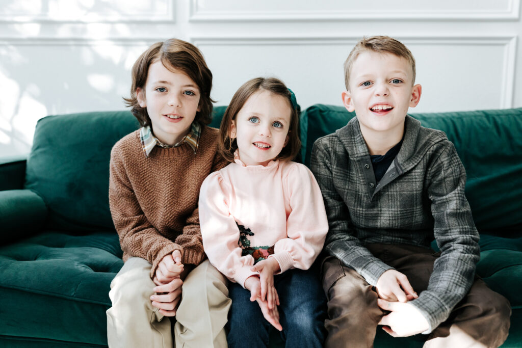Three siblings sitting together on a green couch, demonstrating how photography mini sessions capture simple, timeless portraits.