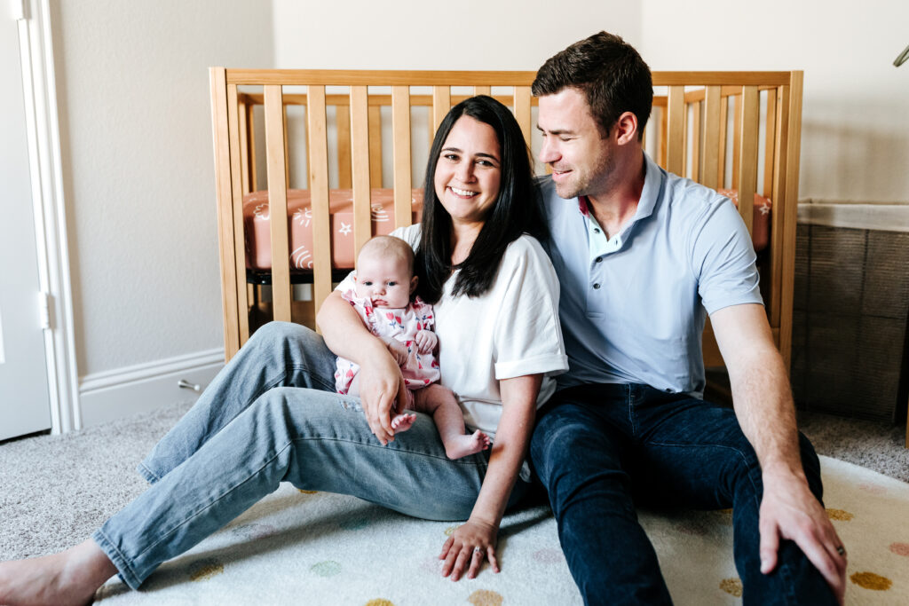 Parents sitting on the nursery floor with their newborn, reinforcing why you should offer mini sessions as a photographer for at-home lifestyle memories.