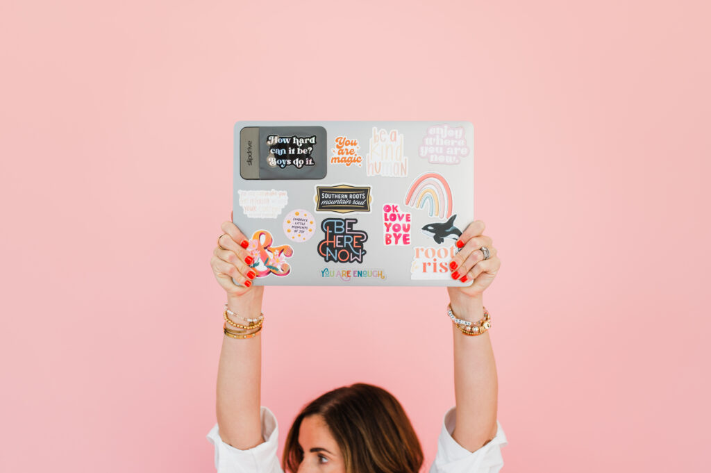 Batching for Photographers: How to Reclaim Your Time 3 Sabrina Gebhardt holding a laptop covered in motivational stickers, sharing her tools and mindset tips for batching for photographers.