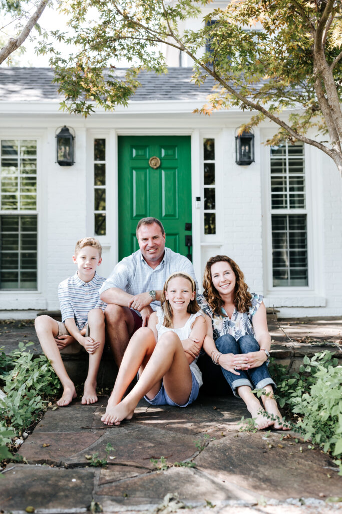 The Best Time of Year to Schedule Family Photos with a DFW Family Photographer 1 Relaxed outdoor family portrait by a DFW Family Photographer, showcasing connection and joy in front of a bright green door.