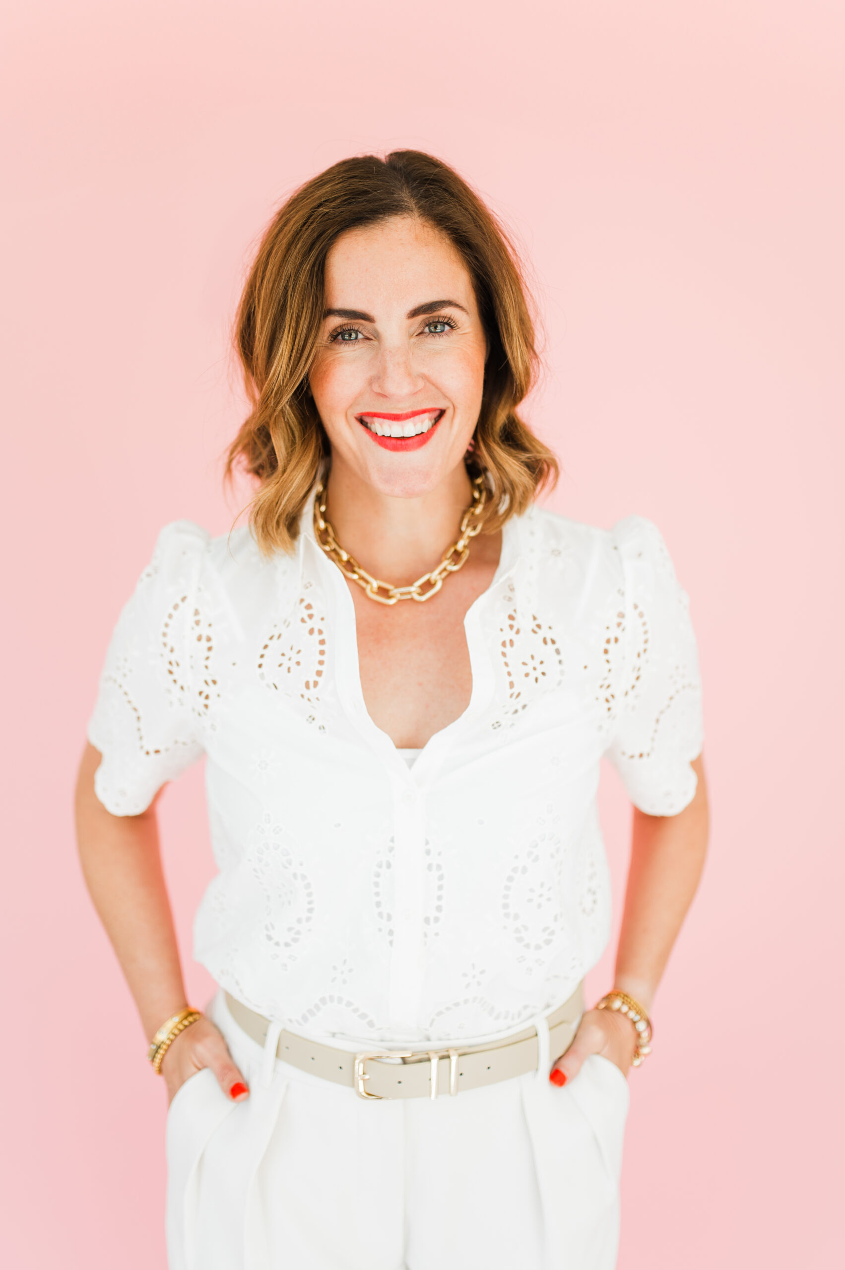Smiling woman in a white blouse with hands in pockets against a pink background, ready to share email marketing for photographers tips.