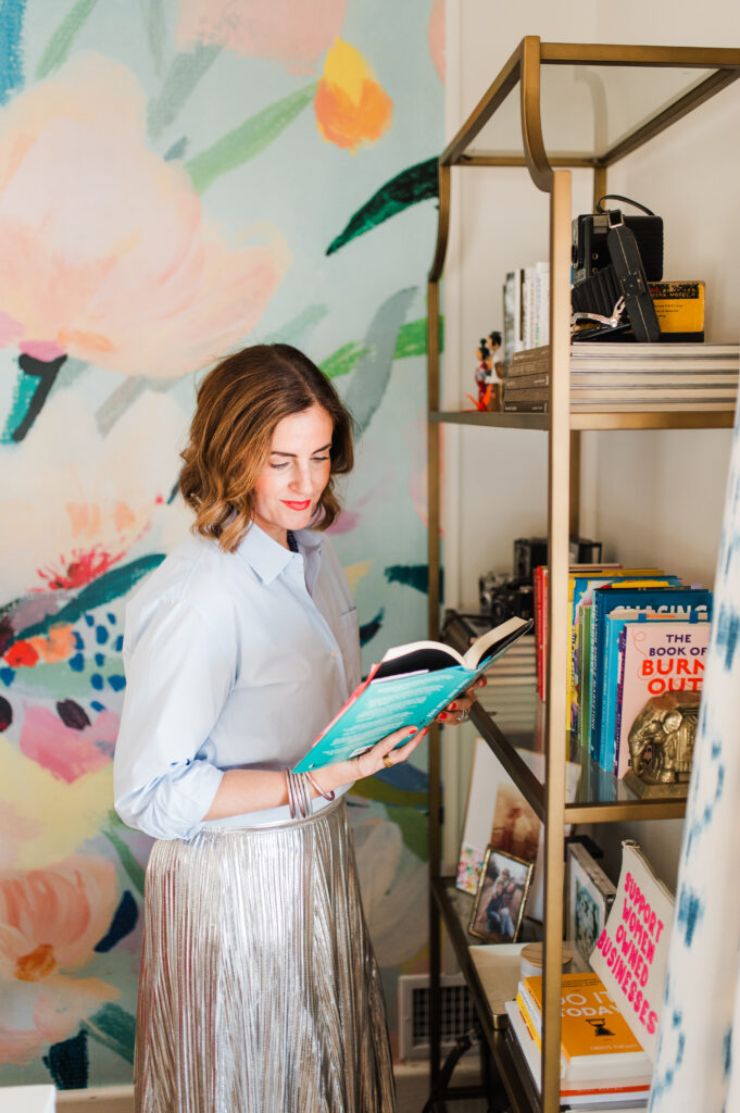 Raise Your Prices With Confidence: How to Know When It’s Time (and Do It Without Guilt) 1 Sabrina Gebhardt reading a business book in her colorful office, encouraging photographers to raise your prices with confidence and clarity.