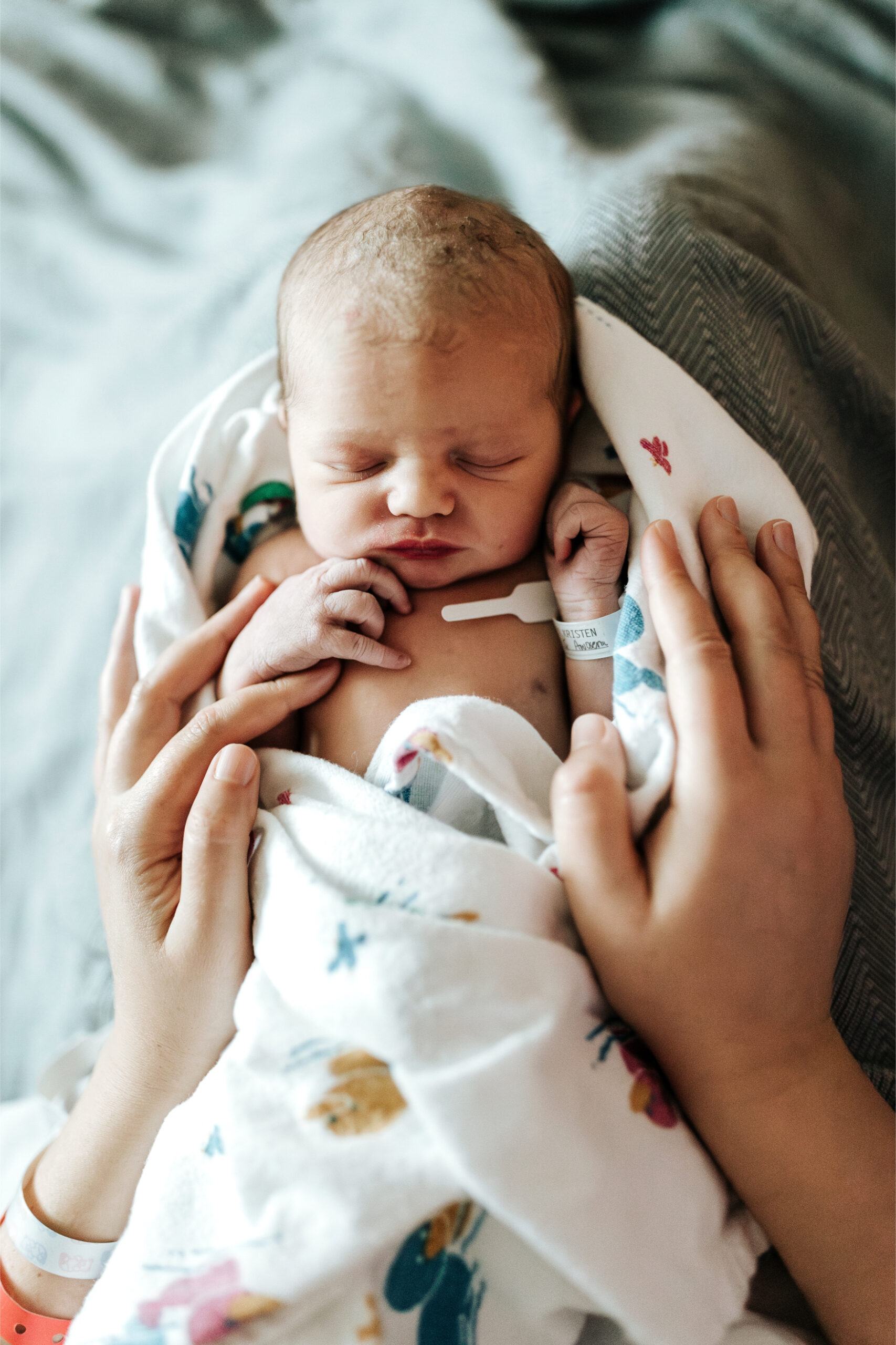 Parent’s hands gently holding a newborn baby wrapped in a hospital blanket during a quiet moment.