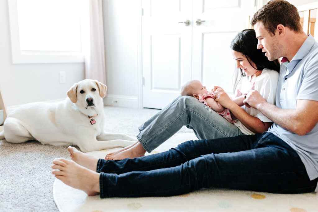 How to Create a Stress-Free Newborn Session at Home 8 Family sitting on the nursery floor with their baby and family dog during a relaxed newborn session at home.