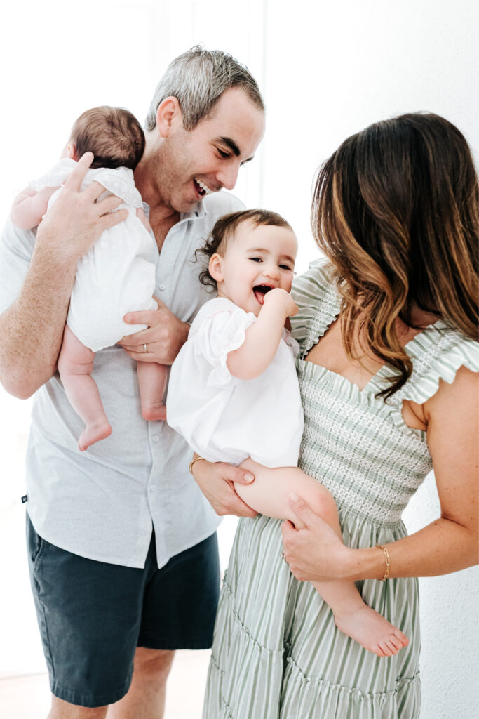 How to Create a Stress-Free Newborn Session at Home 2 Parents laughing with their two children—one toddler and one infant—during a joyful at-home newborn session.