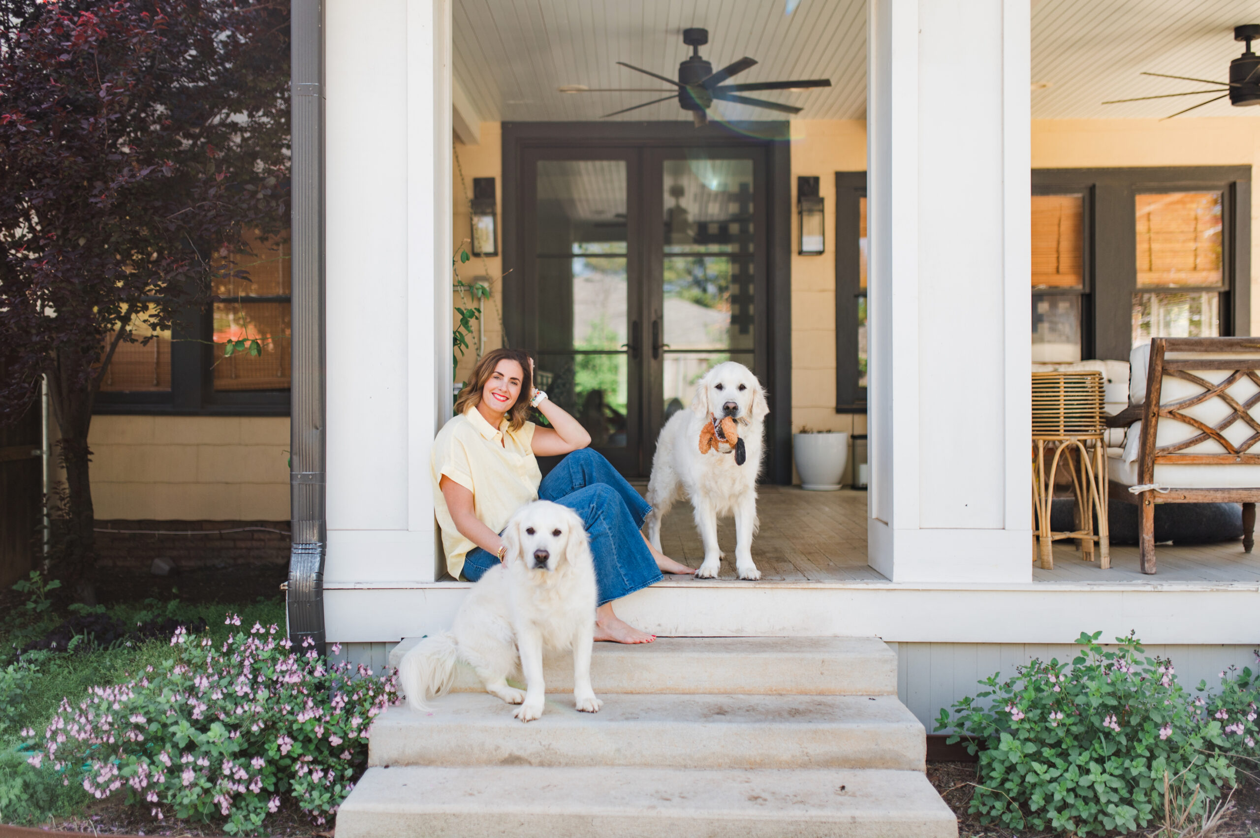 Woman sitting on her front porch with two white dogs, smiling as part of her photography journey.