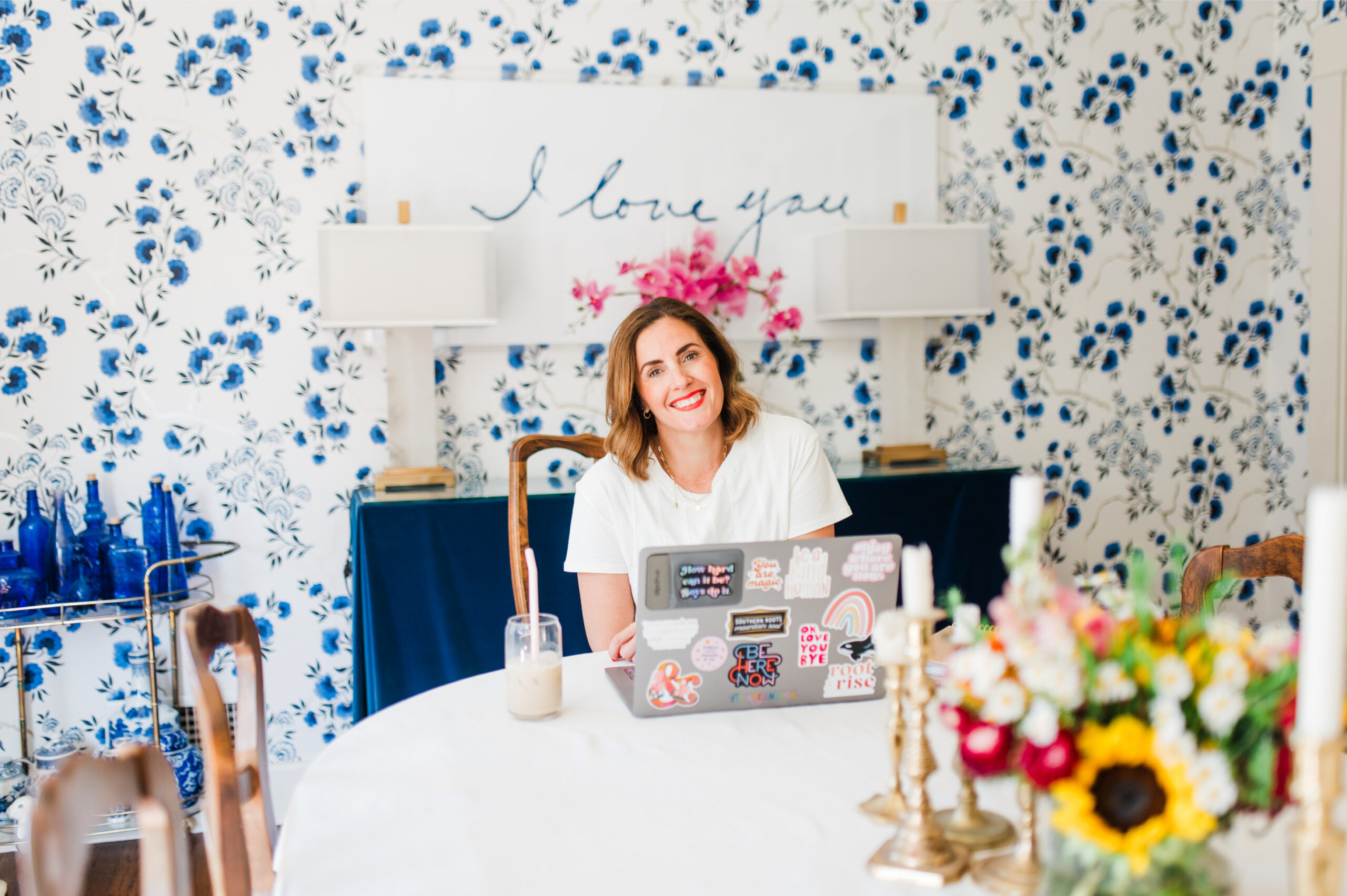 Your Photography Journey: Reflect and Reset for a Fresh New Year 5 Woman working on a laptop at a dining table with floral wallpaper, reflecting on her photography journey.