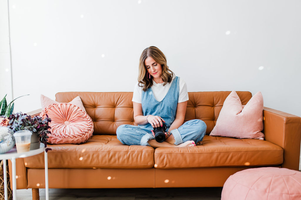 Photographer sitting on a leather couch holding a camera, thoughtfully reflecting on important photography questions.