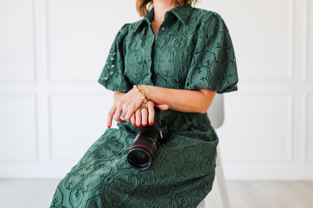 Close up of a woman in a green dress holding a camera, symbolizing confidence in her craft and awareness of pricing mistakes photographers make.