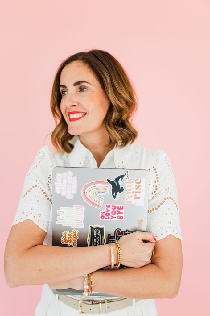 Photographer smiling while holding a sticker-covered laptop, embracing creativity and a bold photography style.