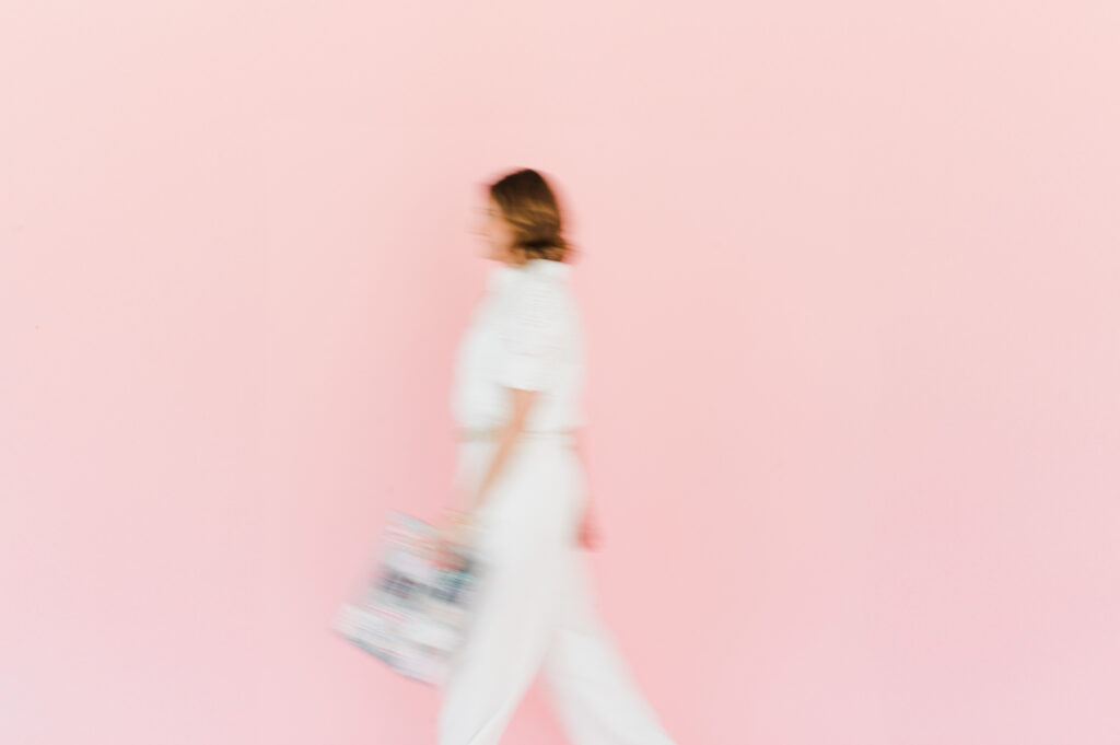 Photographer walking with purpose against a pink wall, symbolizing movement and growth in photography style.