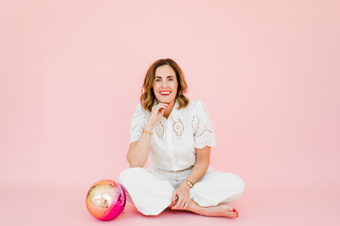 Photographer sitting on the floor with a disco ball, celebrating a fun, vibrant photography style.