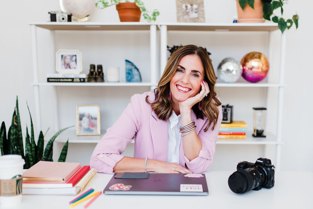 Woman smiling at her desk with camera and laptop while building a photography business from her bright home office