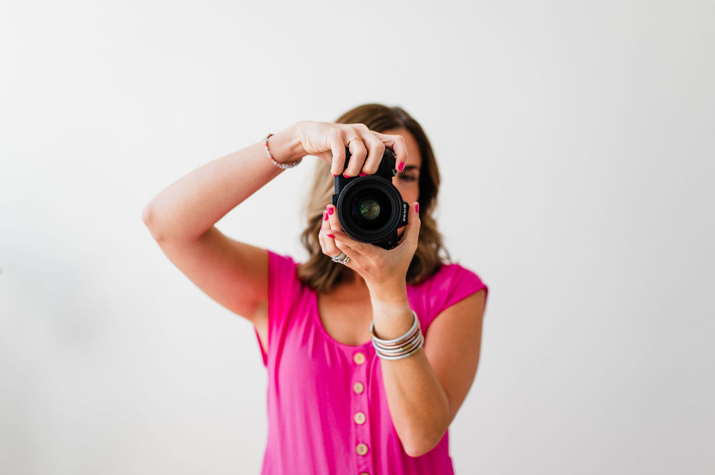 Female photographer holding camera up to her face, capturing her journey of building a photography business