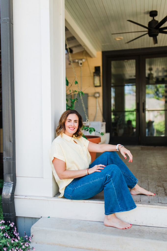 Female photographer sitting barefoot on a front porch, smiling and relaxed in a casual lifestyle brand photo