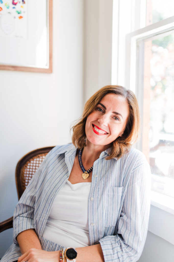 Portrait of a smiling woman sitting by a window with soft natural light, representing calm confidence and tips for photographers
