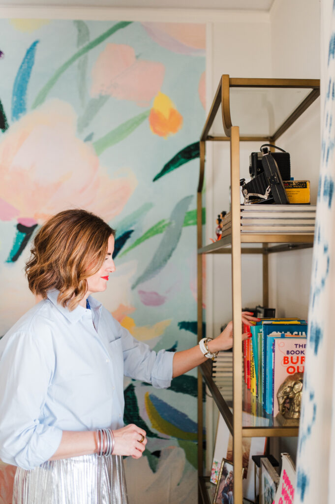 Photographer organizing books on a shelf with a colorful mural wall, creative workspace moment showing tips for photographers