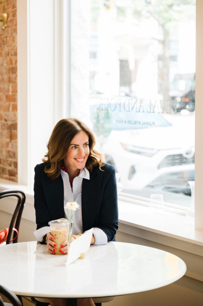 Overcoming Self Doubt as a Photographer: How to Build Confidence Behind the Camera 3 Female entrepreneur sitting in a bright coffee shop holding iced coffee during a relaxed personal branding photography session.
