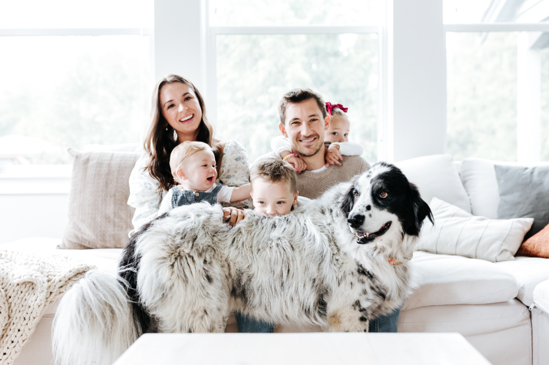 Family of five sitting on a couch with their large dog, smiling and interacting naturally during an in-home session