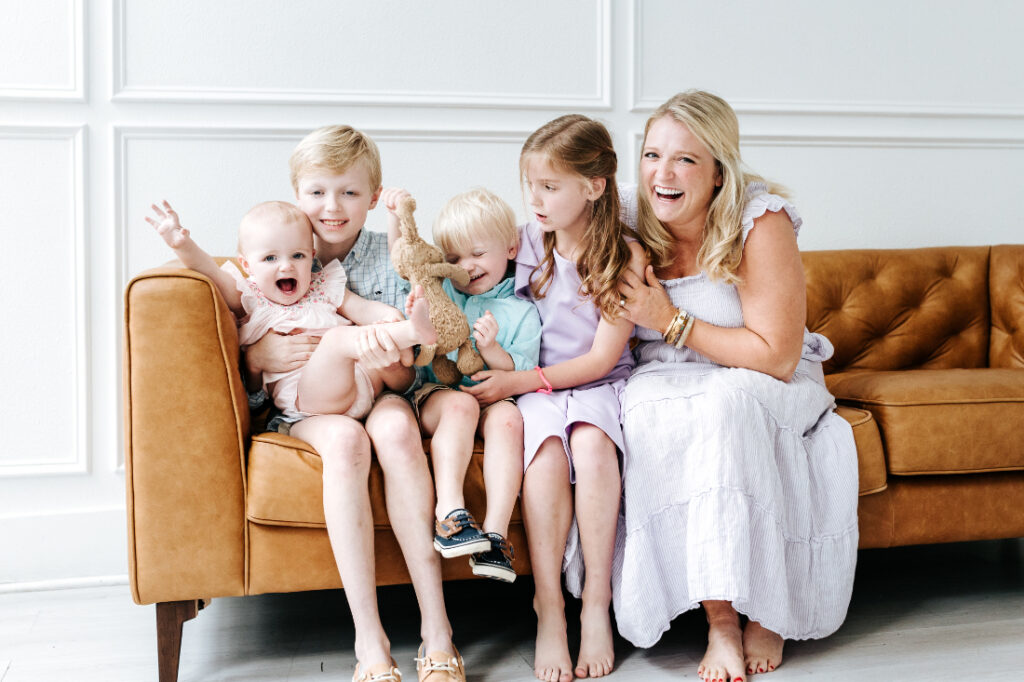 Mom laughing with four young children sitting closely together on a couch during a lifestyle family session