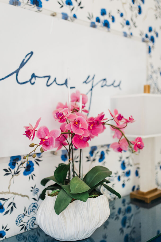 Pink orchids in Sabrina Gebhardt’s bright workspace with blue floral wallpaper and an I love you sign.
