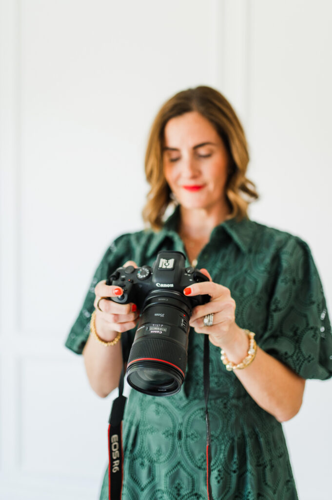 Photographer holding a Canon camera while using a photo editing platform to simplify her editing workflow.