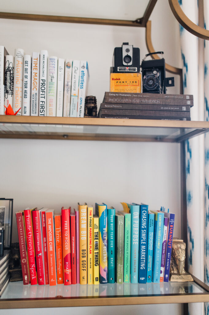 Colorful collection of photography, marketing, and business books displayed alongside vintage cameras on a home office bookshelf.