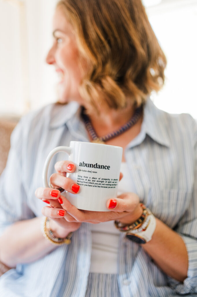 Close-up of a business owner holding a white mug that reads “abundance” while sitting in her bright home.